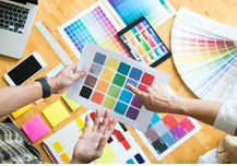 Diseñador discutiendo con un cliente la elección de colores para el próximo proyecto de pintura en Victoriaville. Sobre la mesa hay varias paletas de colores, un ordenador portátil y un teléfono inteligente.