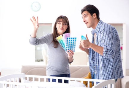 Pregnant woman with her husband in Victoriaville. They are near a crib. They are discussing the choice of color of the room for the soon-to-be-born child. The woman is holding a color palette in her hands.